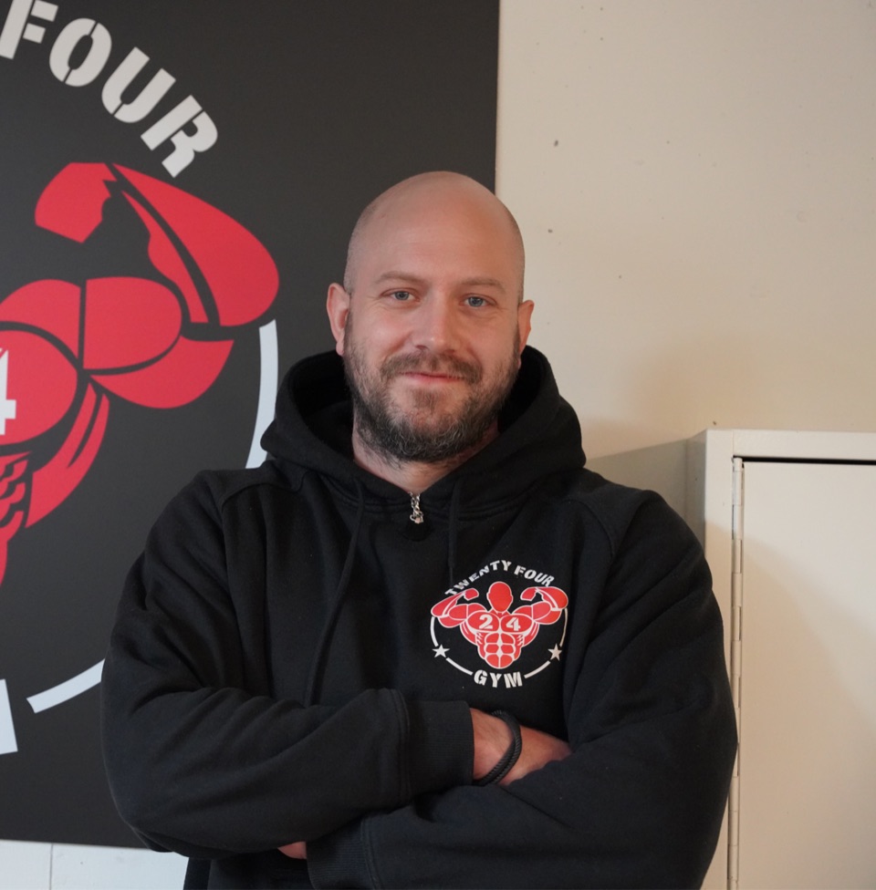Christian Bohny, Geschäftsführer des 24Gym Thun, vor dem Logo des Fitnessstudios